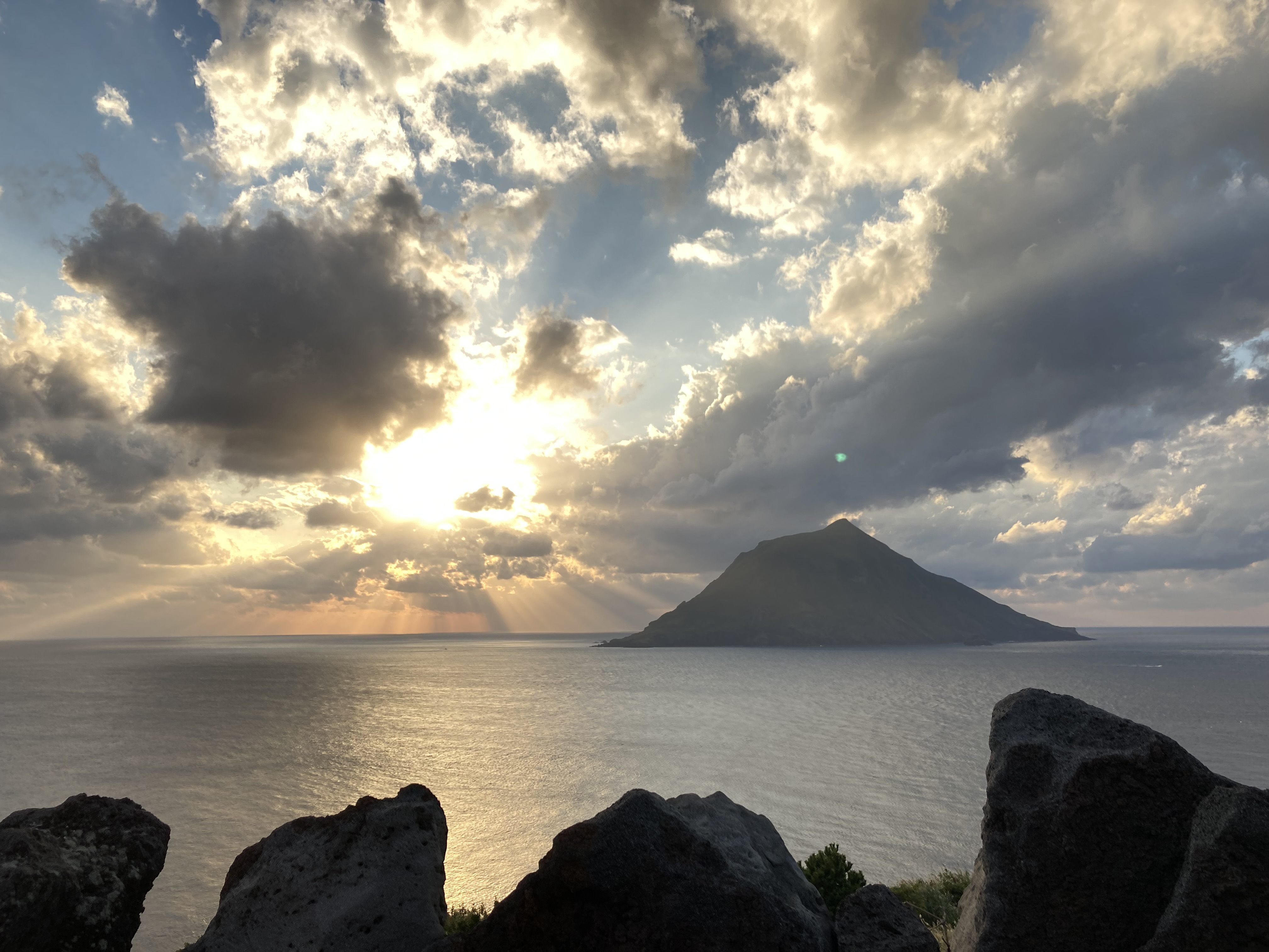 周囲わずか8.7km、聖と俗が交錯したかつての流刑地「八丈小島」：八丈小島の歴史：かつて八丈小島には「鳥打（とりうち）」「宇津木（うつぎ）」という２つの集落がありました。「鳥打」の名は伊豆諸島にゆかりのある平安時代の武将・源為朝に由来するといわれ、古くからこの地が知られていたことがしのばれます。八丈本島〜八丈小島間は約7.5kmとほんのわずか。しかし、間には激しい海流があり、昔から行き来は困難でした。こうした事情などから、高度経済成長期に八丈小島は日本の発展に取り残されるような形になります。1966年（昭和41年）、住民たちは過疎化や子弟の教育に対する不安もあり、ついに離島を決意します。これが八丈町・東京都に認められ、1969年（昭和44年）には全国初事例となる集団離島が実現しました。現在の八丈小島：全員離島から半世紀を経た現在、かつての集落は廃墟となり、島はふたたび原始の姿に環りつつあります。そんななか、近年島内で準絶滅危惧種・クロアシアホウドリの繁殖が確認され、世界最北の繁殖地となりました。2014年（平成26年）には『八丈小島忘れじの碑』が、八丈小島を臨む南原千畳敷に建立。2019年は離島からちょうど50年を迎え、八丈町で八丈小島にまつわる企画展示や講演会が行われるなど、改めて注目を集めています。八丈小島に上陸するには？：現在でも釣りやトレッキング（※登山道はありません）などで時おり上陸する例はあります。とはいえ、もちろん定期航路もないので、漁船などのチャーターが必要。また現地にも港湾設備がなく、海況のよい時に岩場から上陸する形になります。ということで、基本的に上陸のハードルは高めです。また万が一島内で不測の事態があっても直ちに対応できないため、八丈島観光協会では『八丈小島への渡島ルール』を設けています。『八丈小島への渡島ルール』・八丈小島における宿泊は、禁止されています。・天候が少しでも危ぶまれる際は、八丈小島への渡島は避けてください。・海況の変化に応じて何時でも避難できるよう、渡船を用意してください。『【八丈島】八丈小島』について、アクセス：八丈島よりチャーター船で片道約40分